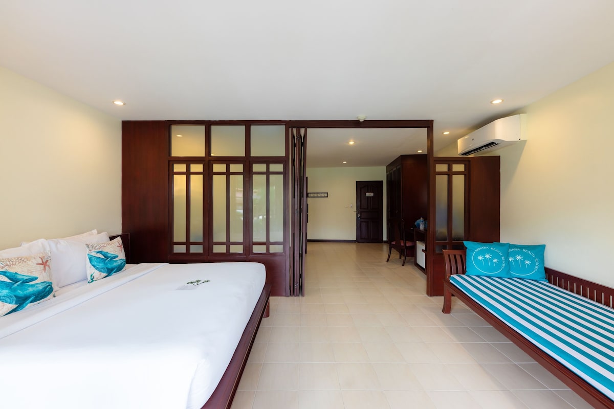 Una habitación de hotel con cama, sofá, separador de madera y aire acondicionado.