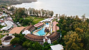 Vue aérienne d’un complexe hôtelier doté d’une grande piscine, d’un accès à la plage et d’une végétation luxuriante.