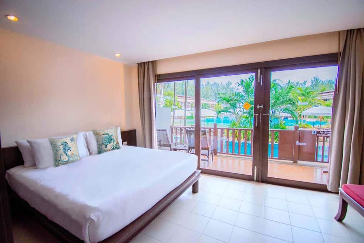Quarto de hotel com uma cama grande, uma varanda com vista para a piscina e uma porta de vidro deslizante.