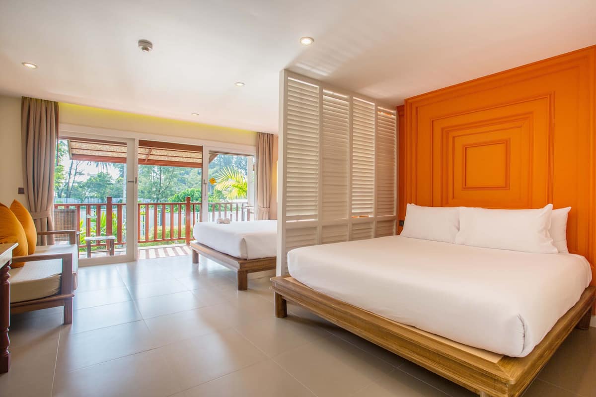 Quarto de hotel com uma cama grande, um sofá e uma varanda com vista para o verde.