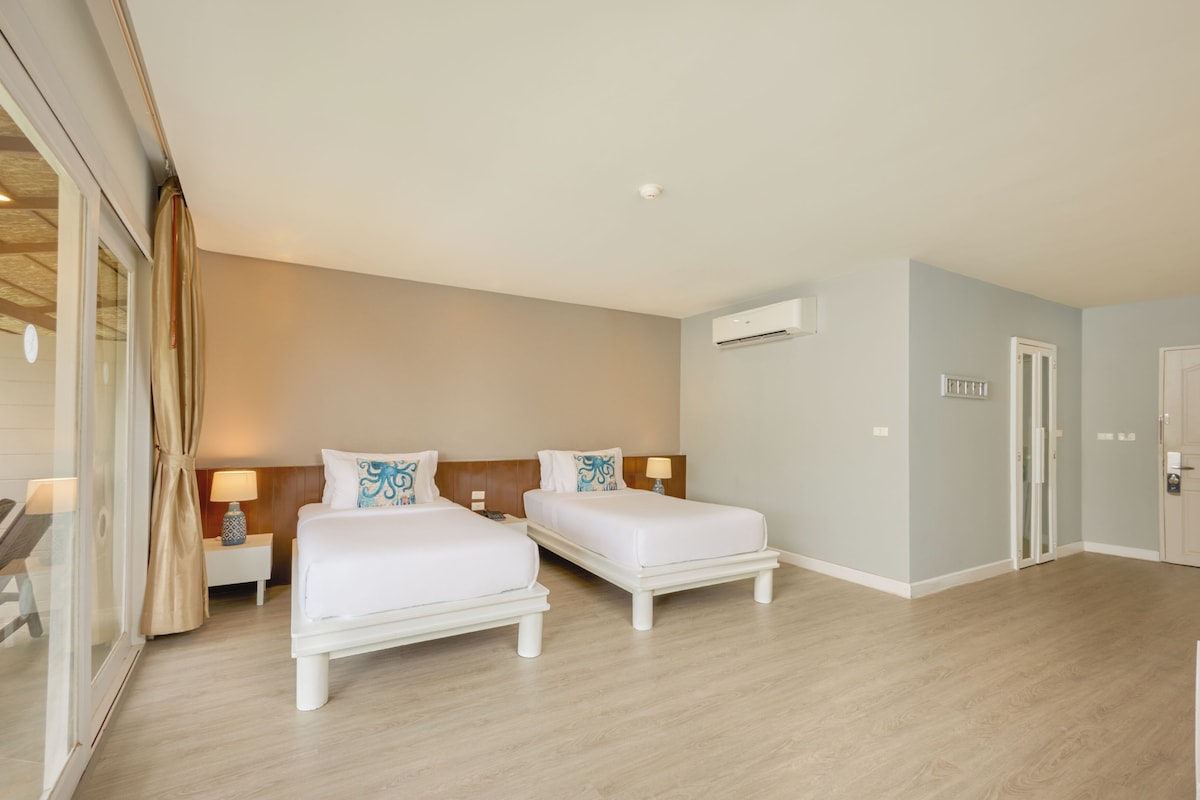 Habitación de hotel con dos camas, un escritorio, una silla y una ventana con cortinas.