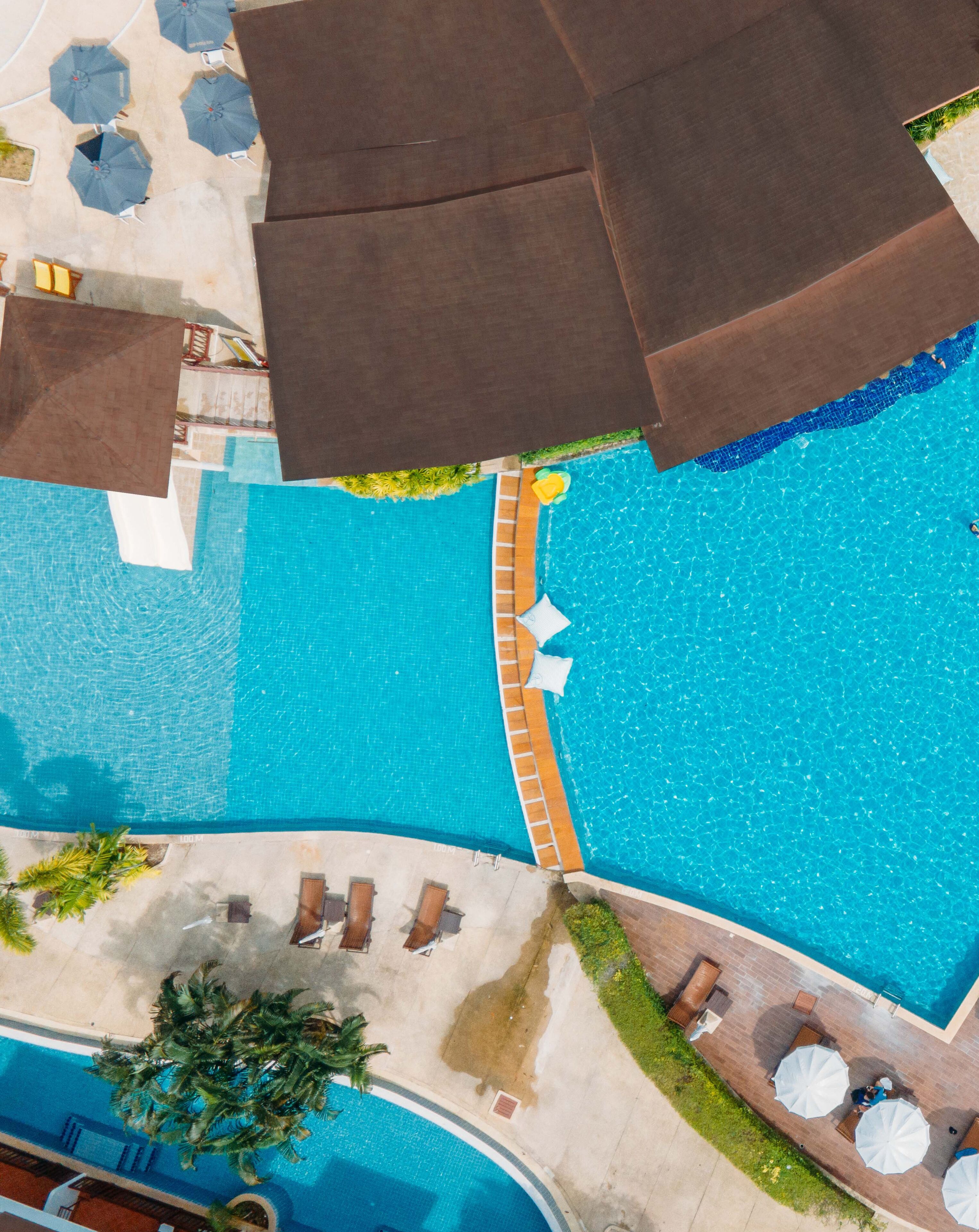 Vue aérienne d’un espace piscine d’hôtel, avec de nombreux transats, des parasols et un petit jardin.