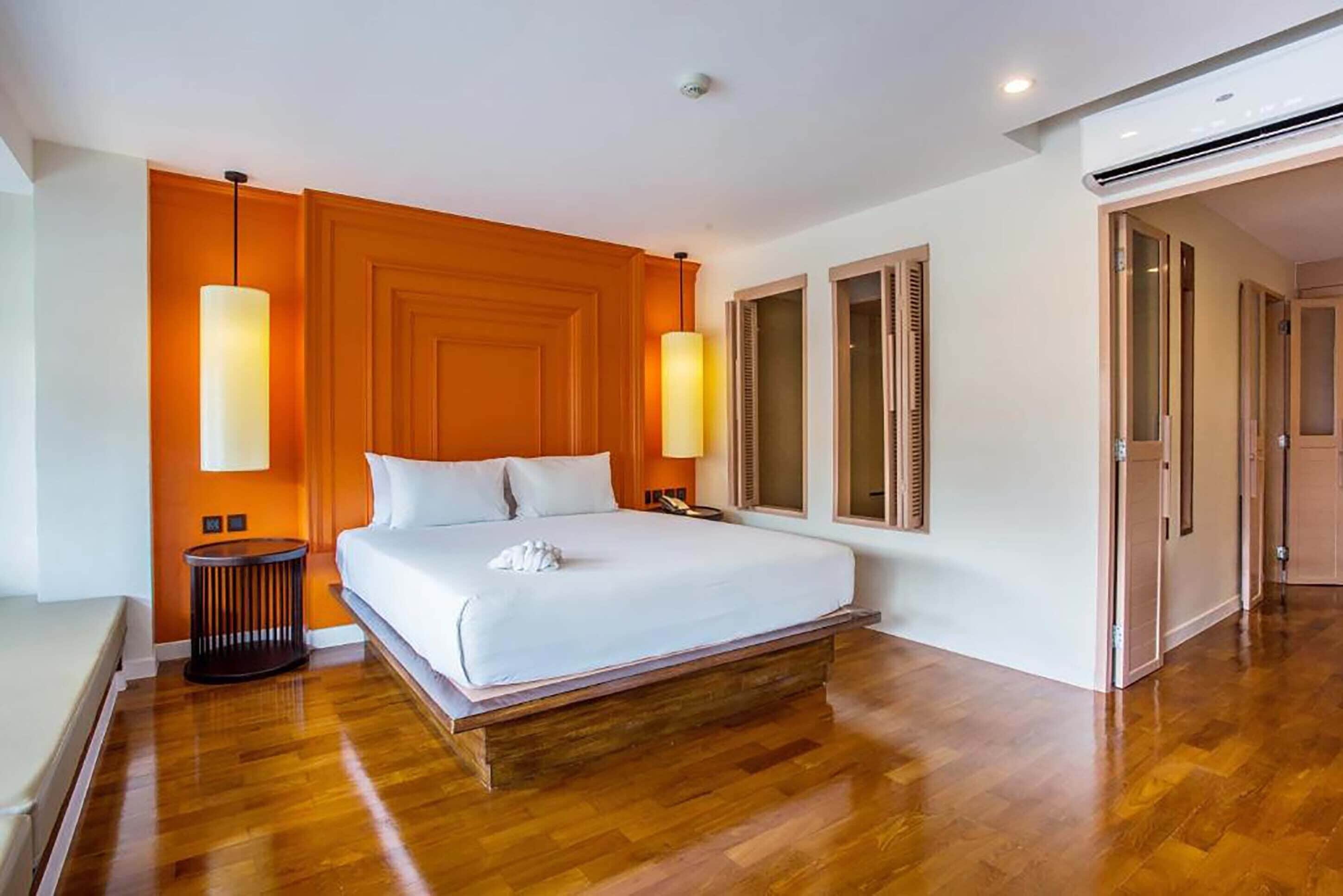 Una habitación de hotel moderna con suelo de madera, una cama grande, dos lámparas de noche y un armario.