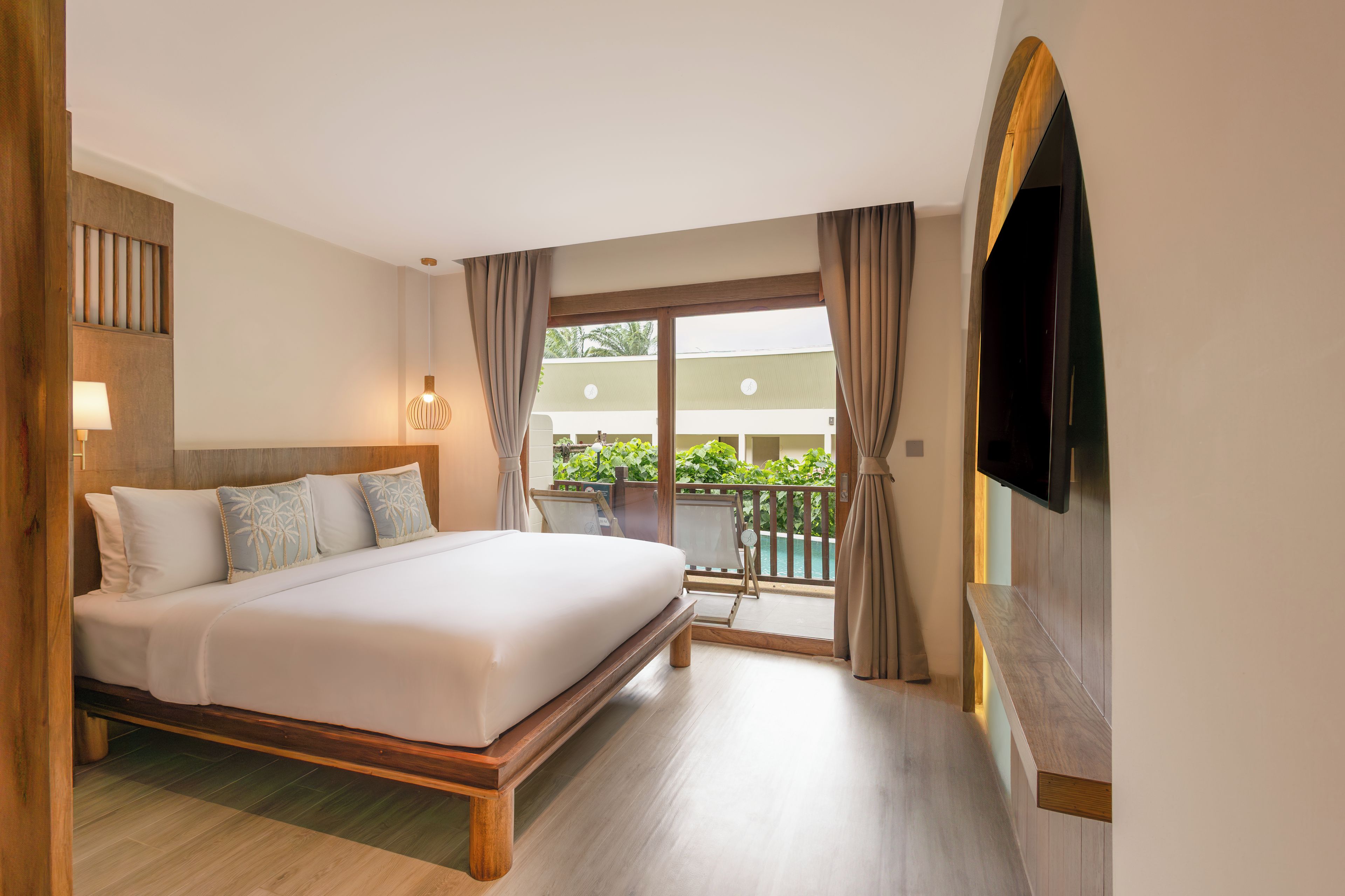 Une chambre d’hôtel avec un grand lit, un téléviseur fixé au mur et un balcon donnant sur un paysage verdoyant.