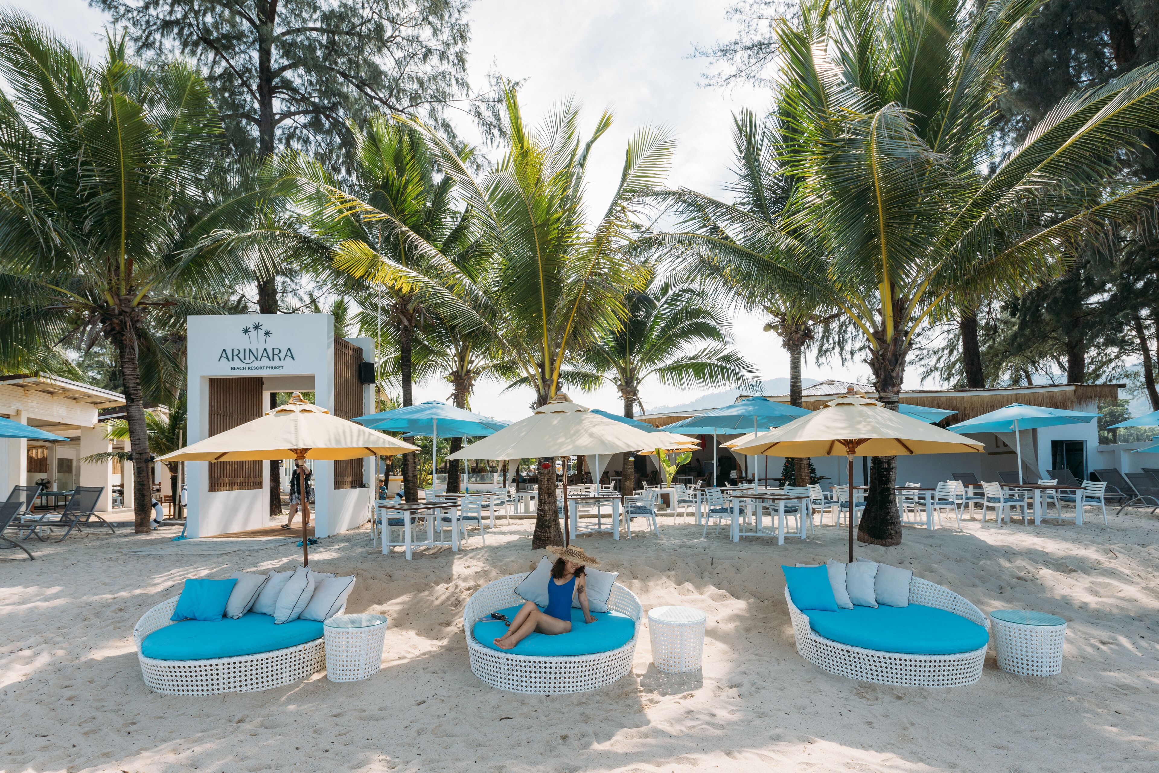 A beach resort with white wicker lounge chairs, blue cushions, and umbrellas.