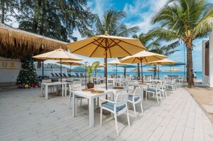 An outdoor seating area with white tables and chairs, large umbrellas, and a Christmas tree.