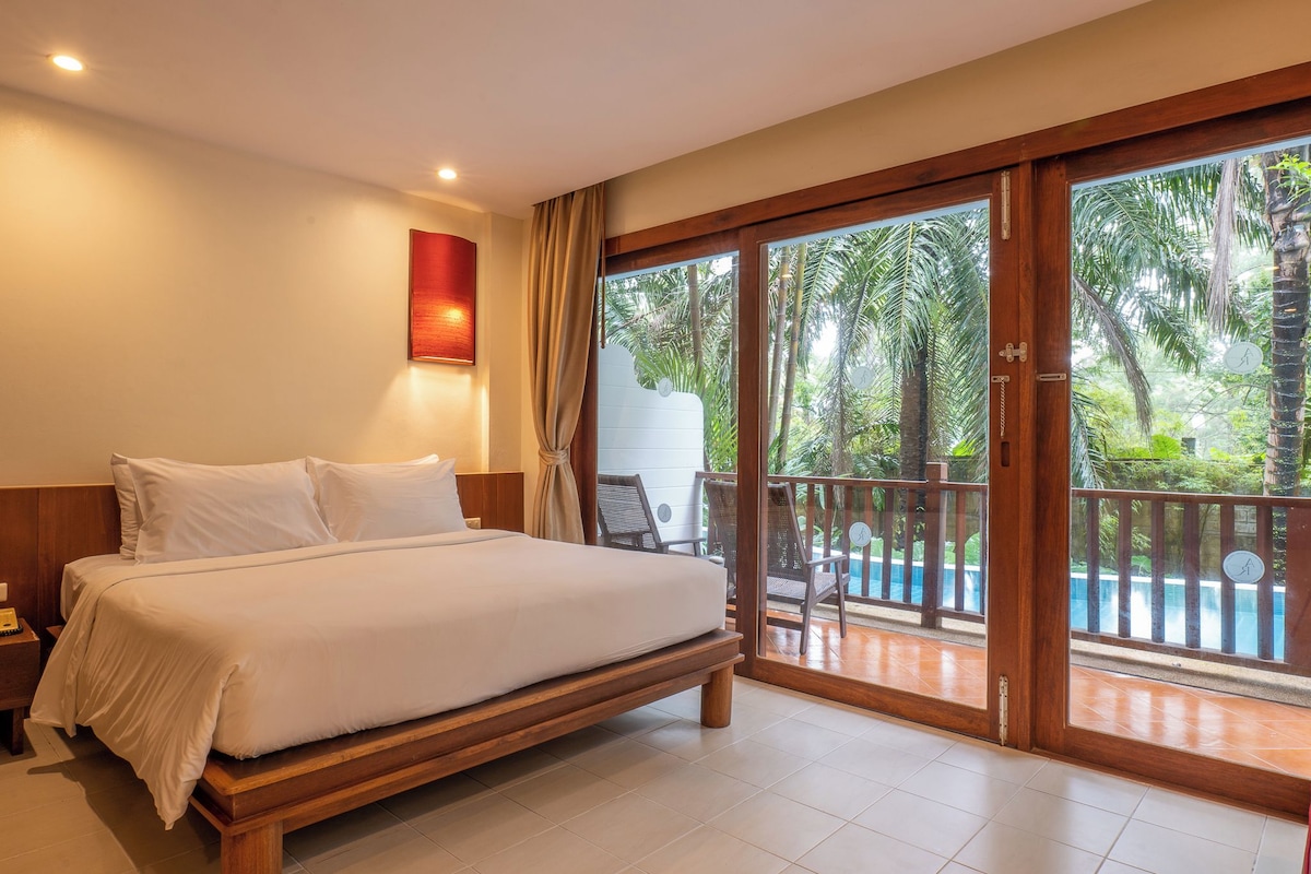 A bedroom with a large bed, a nightstand, a wall-mounted light, and a sliding glass door leading to a balcony with a pool.