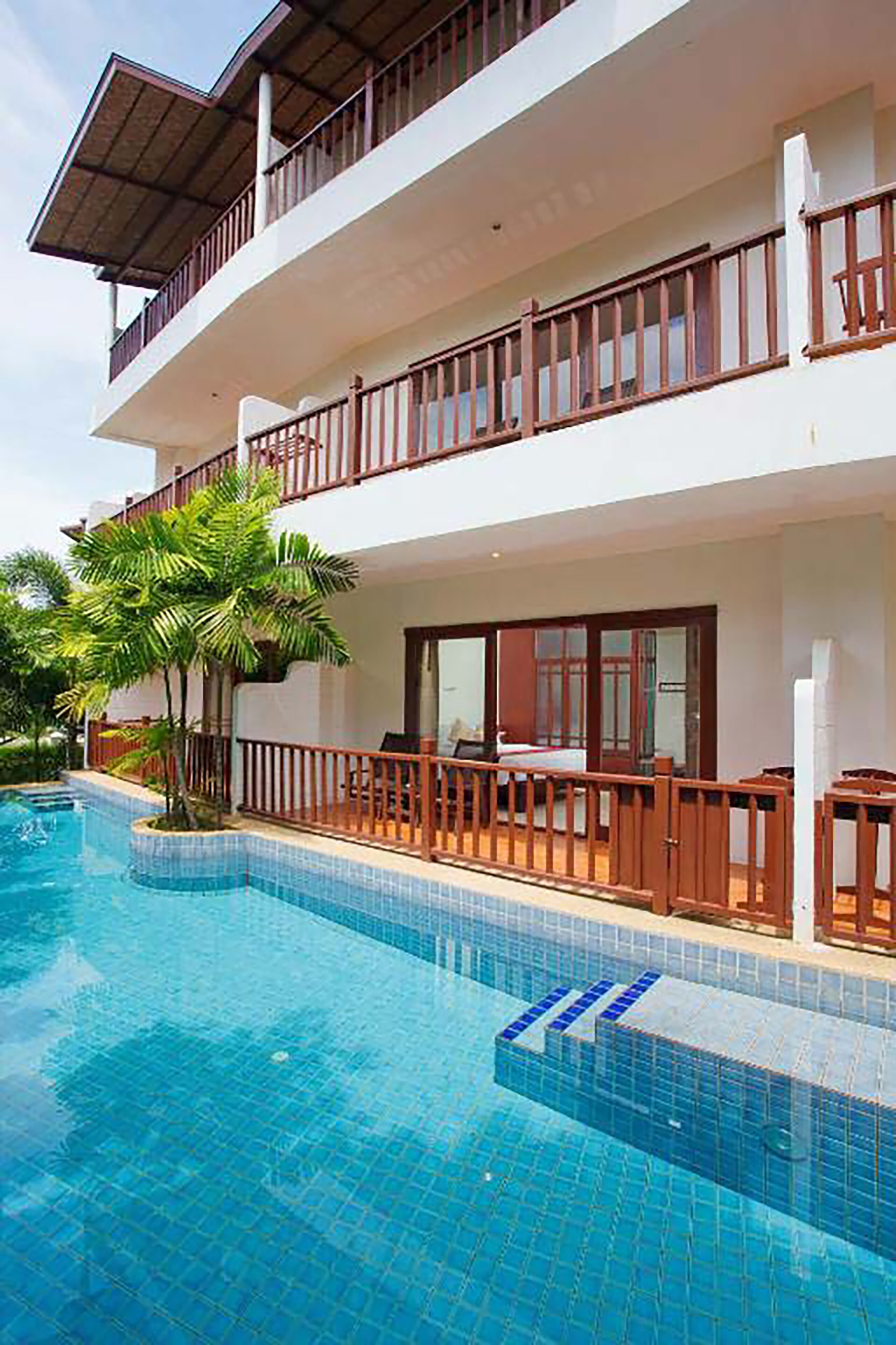 A two-story building with a swimming pool, balconies, and a tropical garden.
