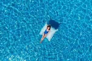 Una persona recostada sobre una toalla a rayas en una piscina azul cristalina.