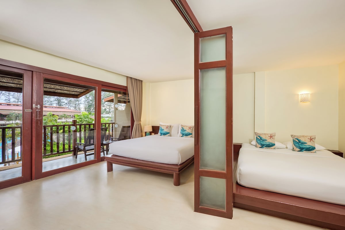 A hotel room with two beds, a balcony with a view of greenery, and a sliding glass door.