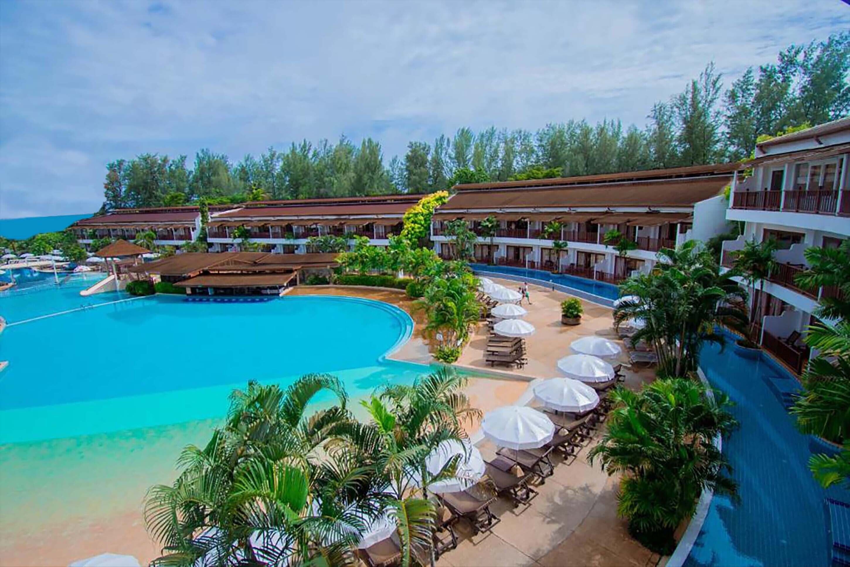 Un complexe hôtelier doté d’une grande piscine, de chaises longues et de parasols.