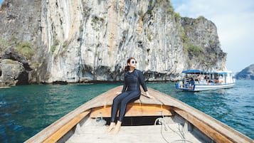 A person sitting on a wooden boat with a rocky cliff in the background.