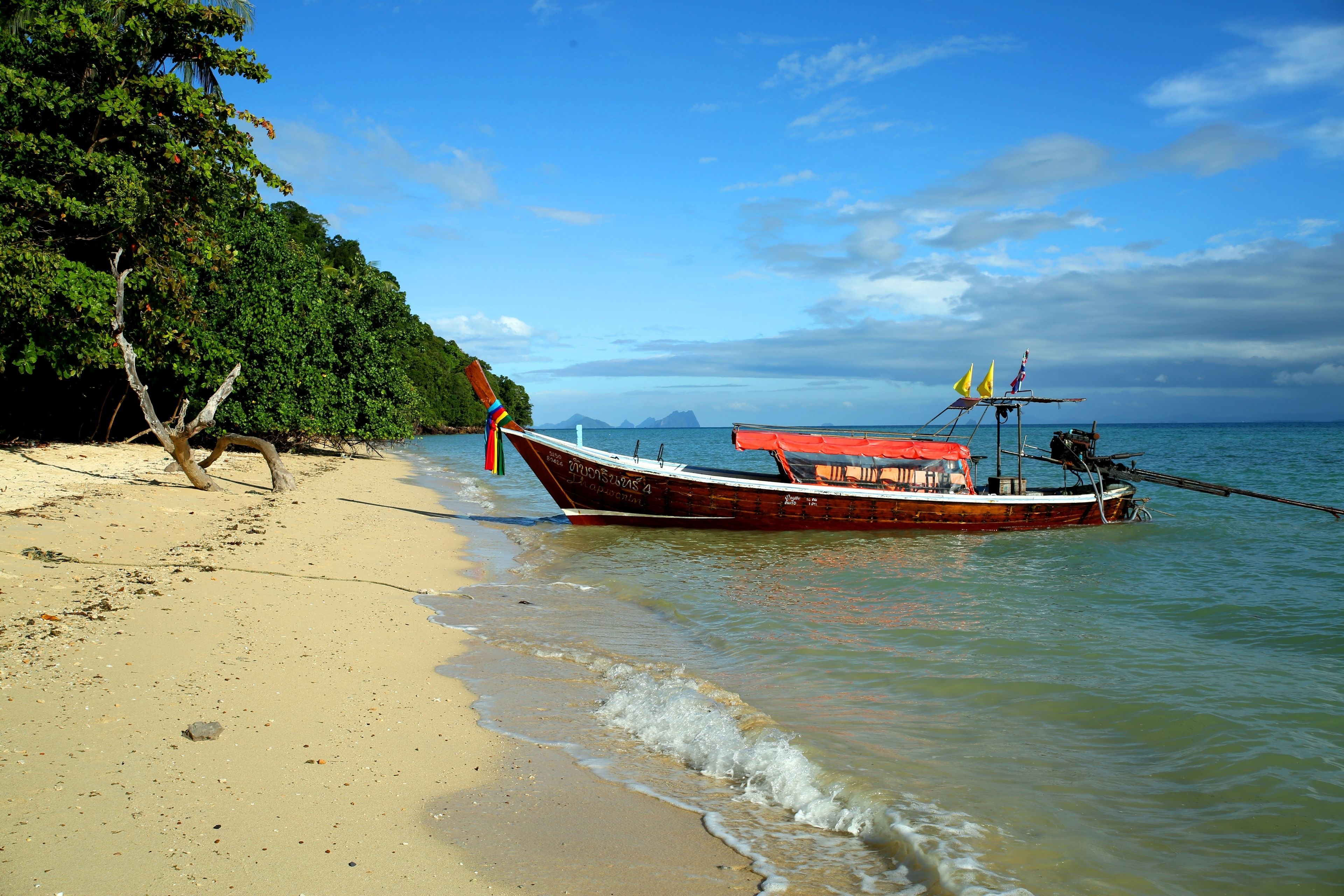A boat anchored on a sandy beach with a forested area and a clear sky in the background.