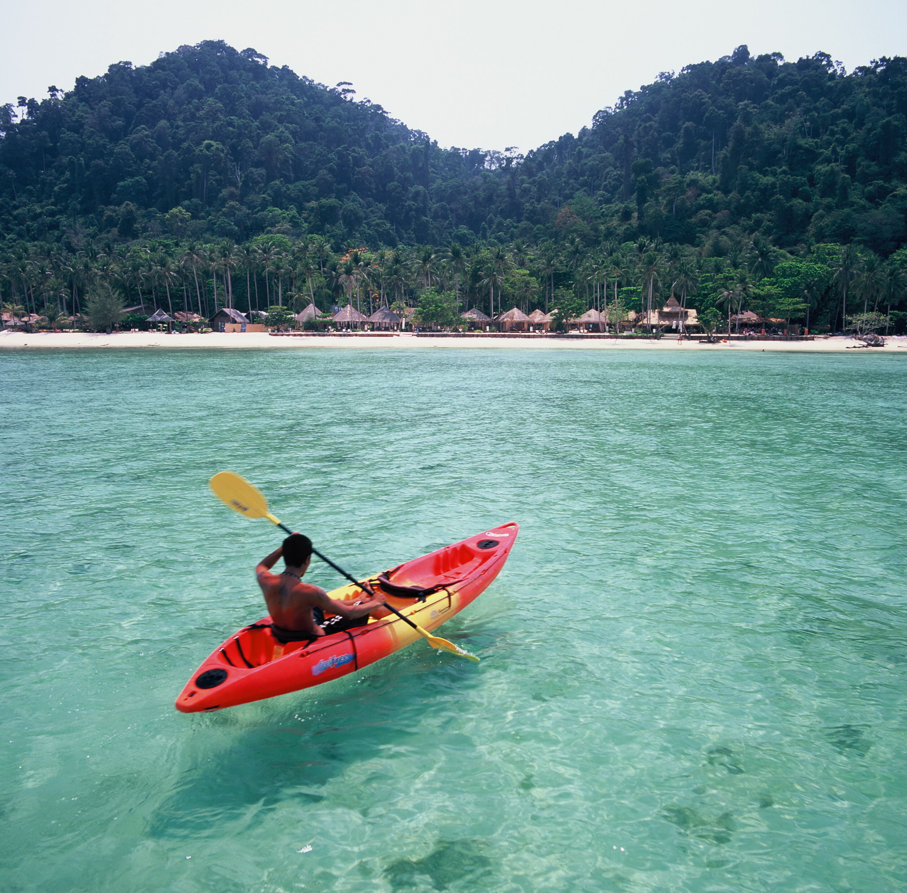 A clear view of a beach with a kayaker in a red kayak.