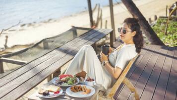 A person sitting on a wooden deck chair with a table in front of them, holding a cup.