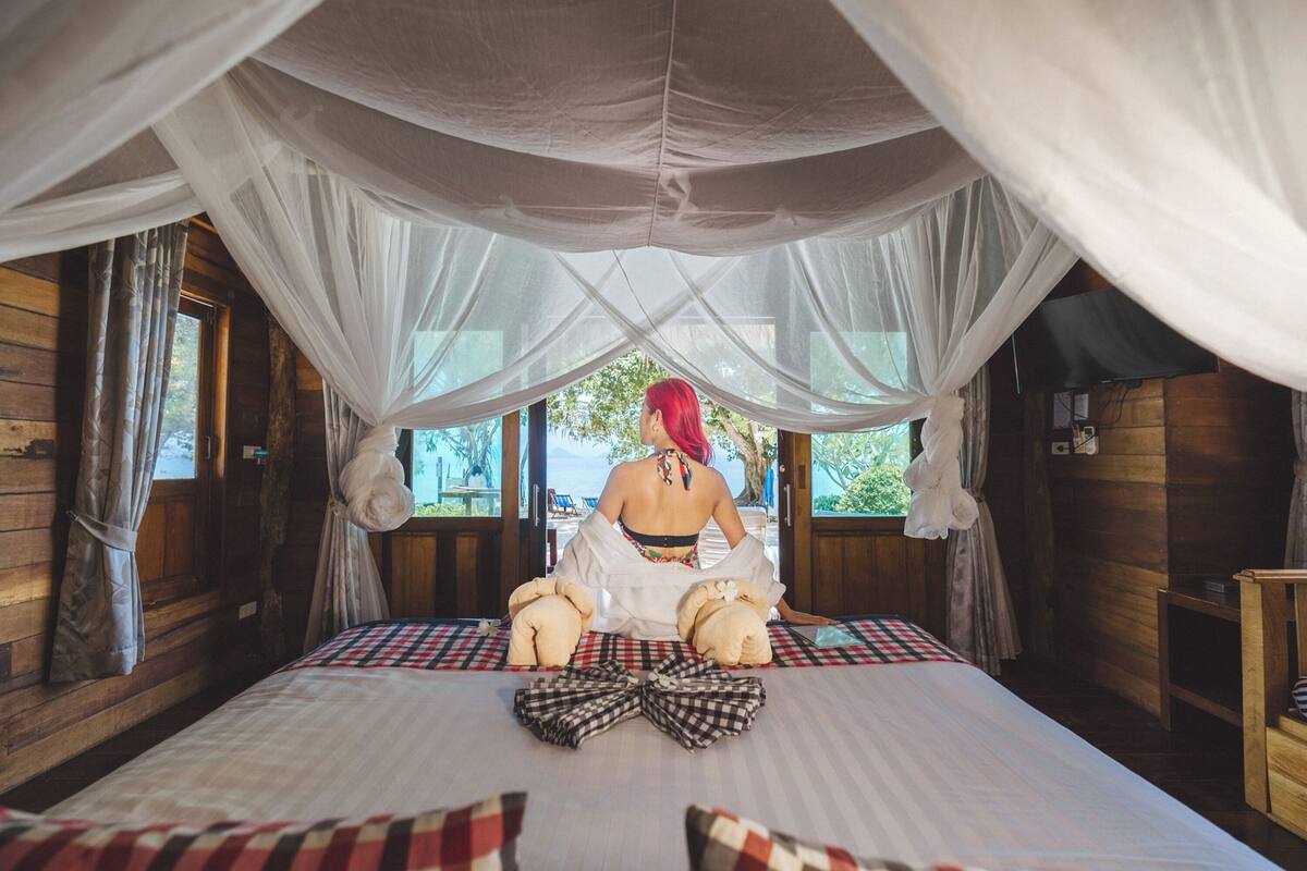 Habitación con cama bajo un dosel, paredes de madera y ventana con vistas.