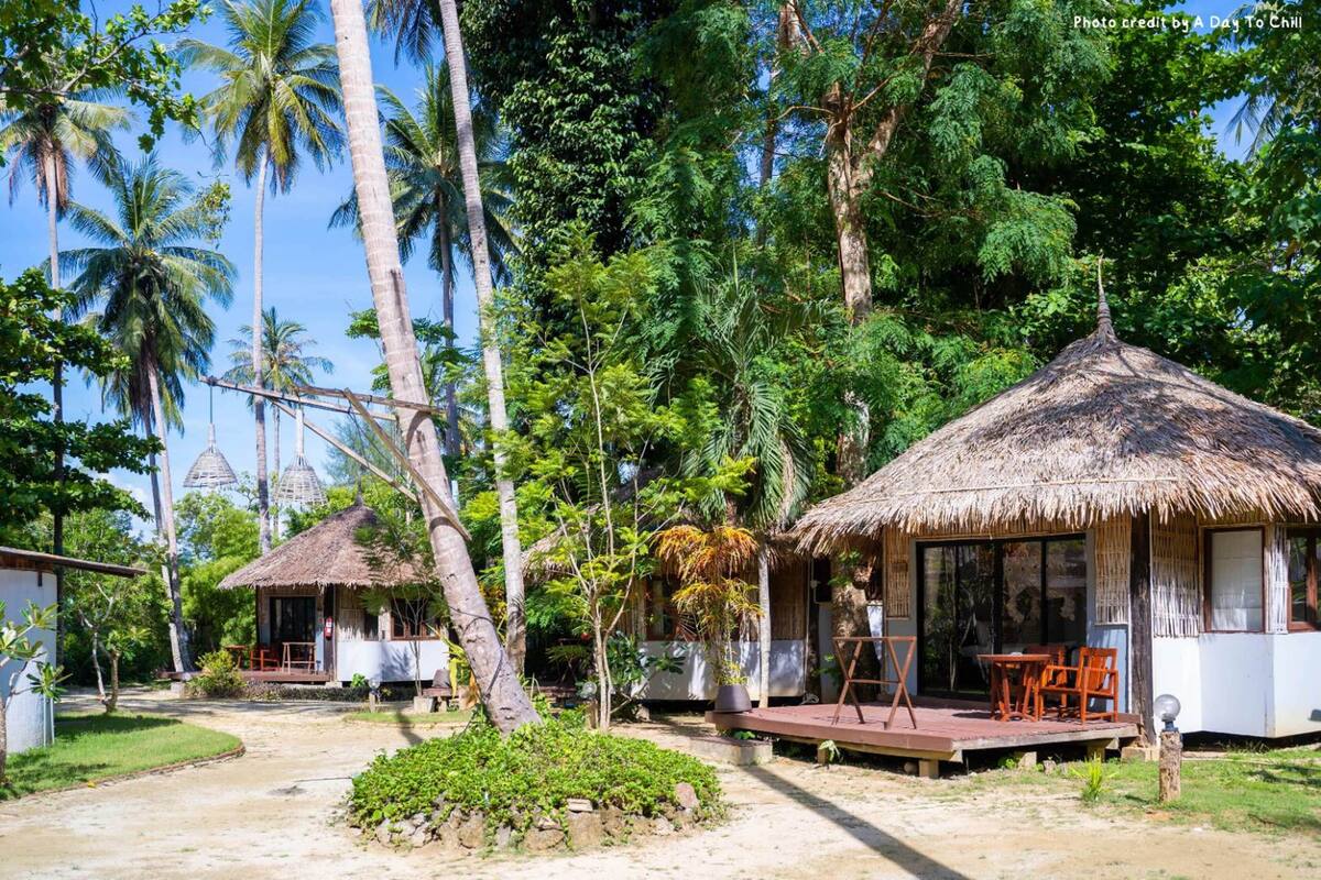 Un resort tropical con cabañas de techo de paja, un sendero pavimentado y abundante vegetación.