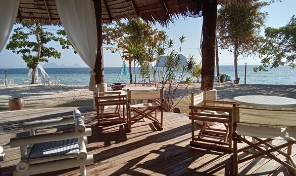 A wooden deck with outdoor seating, overlooking a beach with palm trees and a clear view of the sea. - Mayalay Resort-Green Hotel (Ko Lanta)