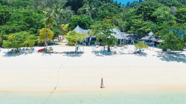 Un resort en la playa con cabañas de techo de paja, una playa arenosa y exuberante vegetación.