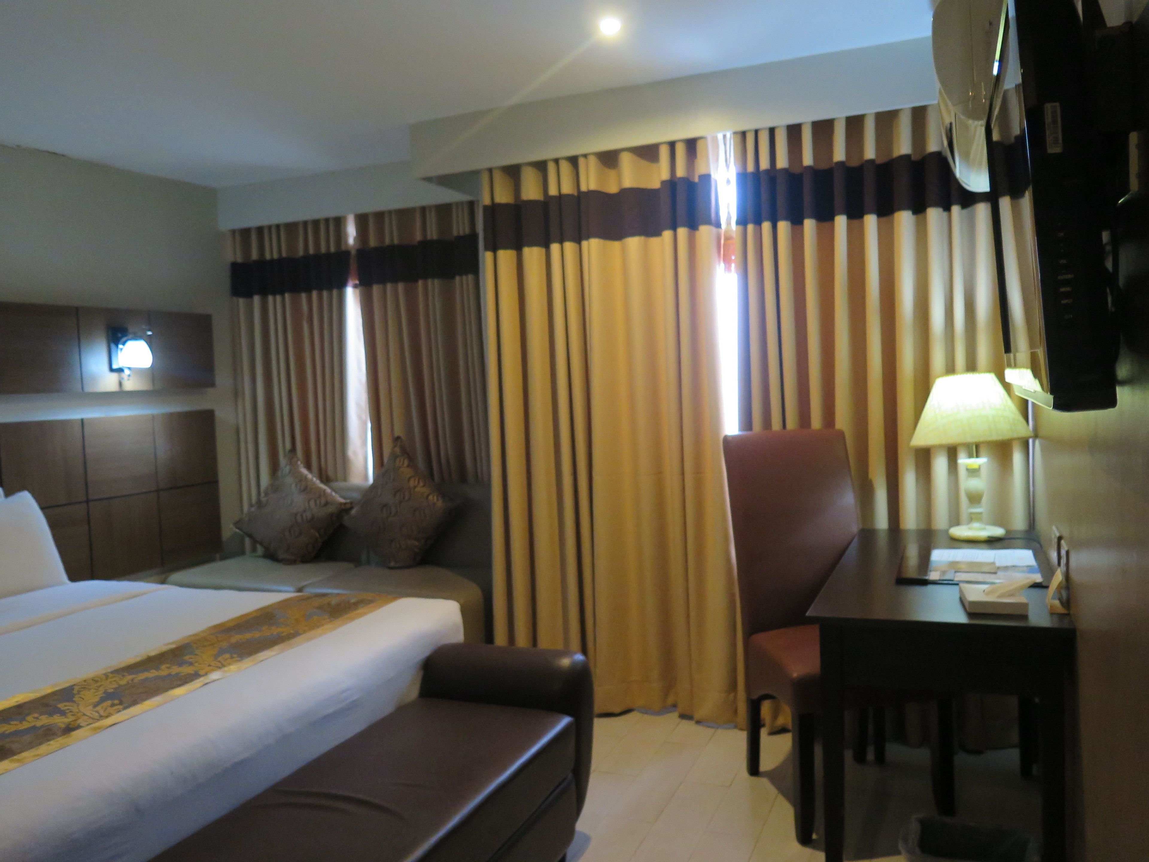 Una habitación de hotel con una cama grande, un escritorio con lámpara, una silla y cortinas.