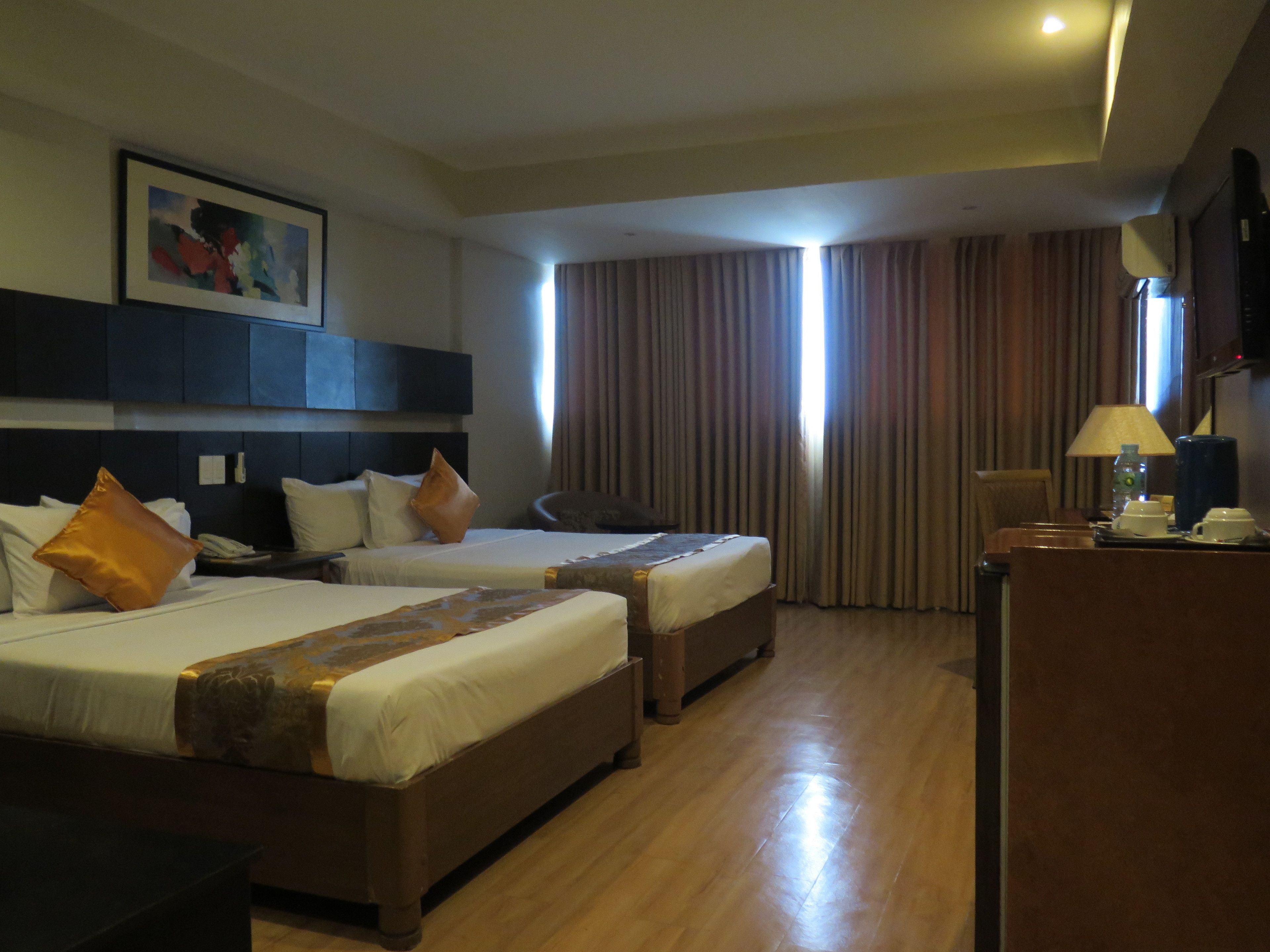 A hotel room with two beds, a desk, a chair, and a large window with curtains.