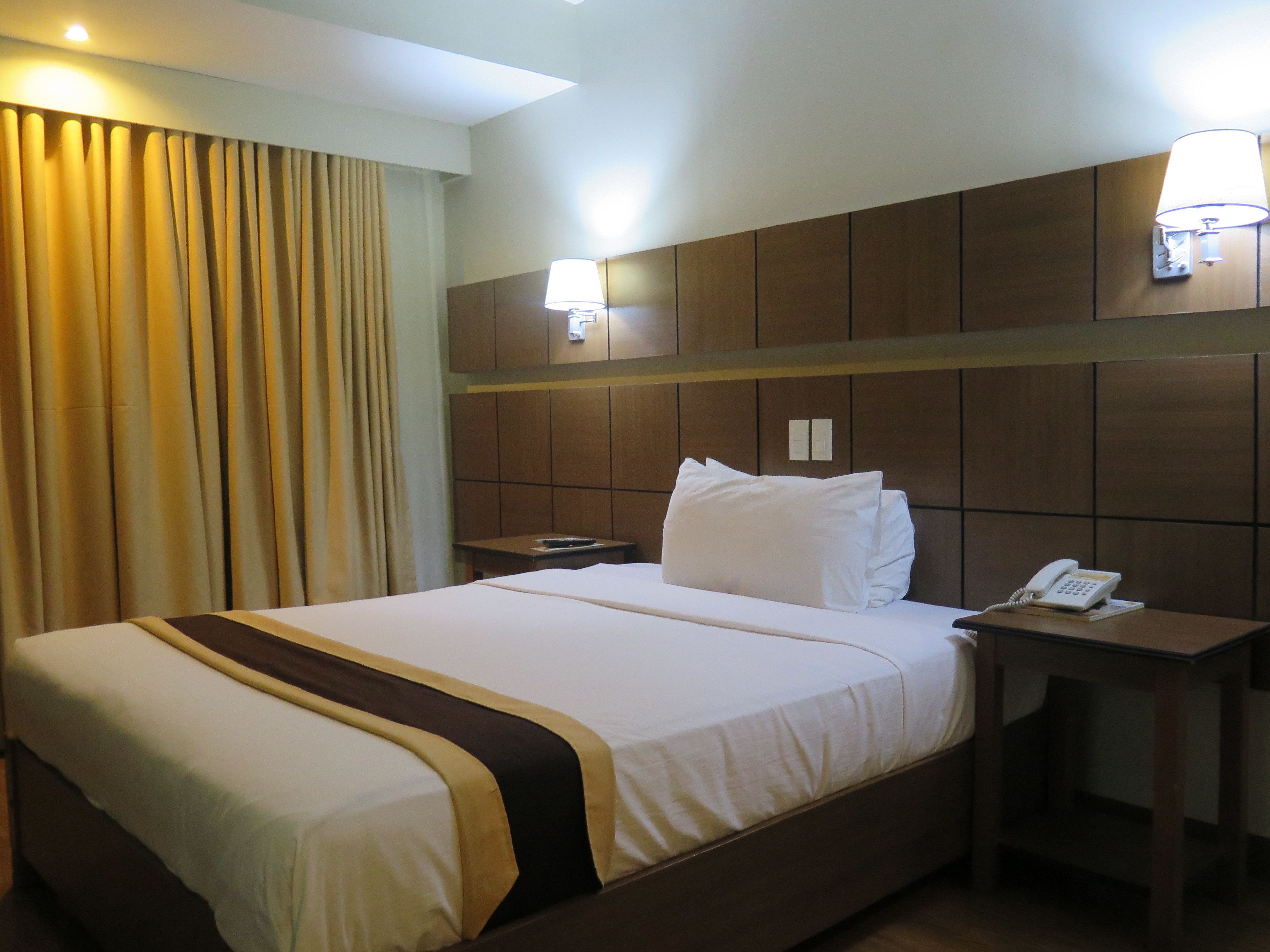 Ein Hotelzimmer mit einem großen Bett, einem Nachttisch mit Telefon und einer Wandlampe.