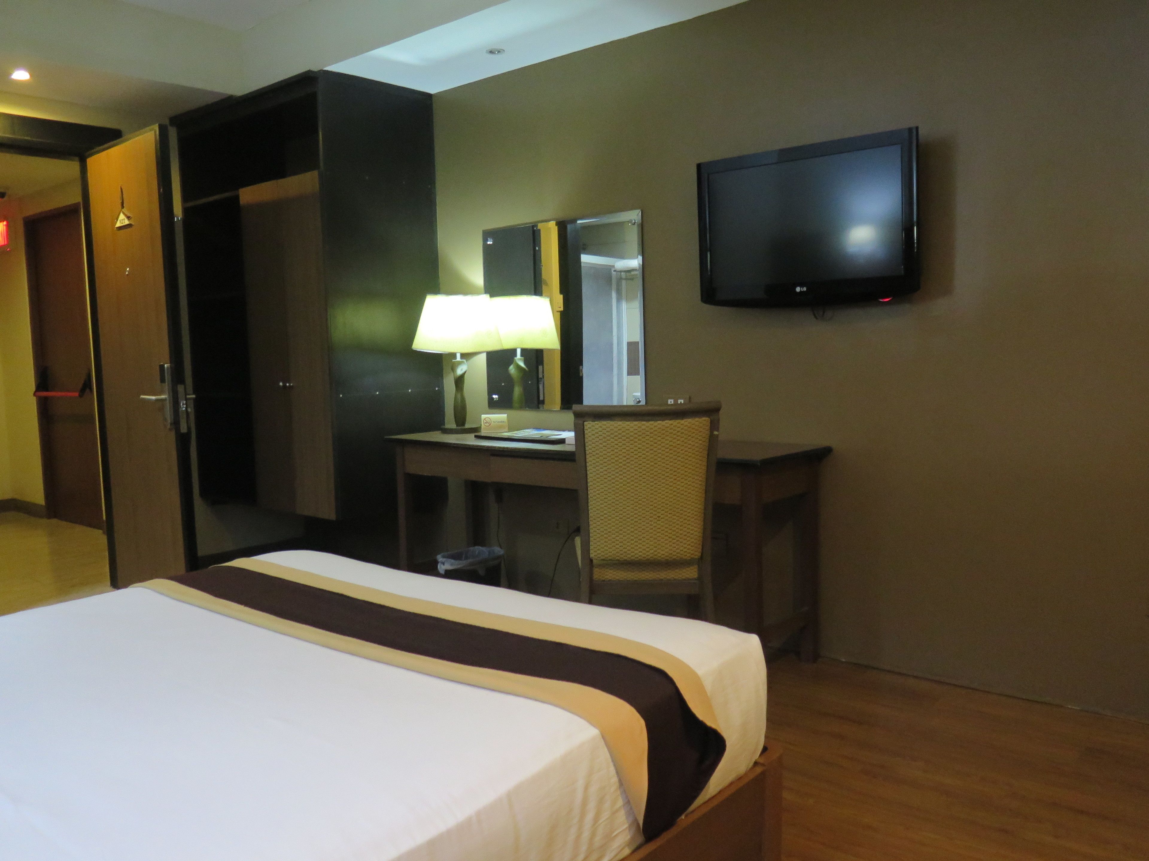 A hotel room with a bed, desk, chair, lamp, television, and wardrobe.