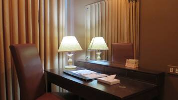 A hotel room with a desk, two chairs, a lamp, a mirror, and a 'No Smoking' sign.