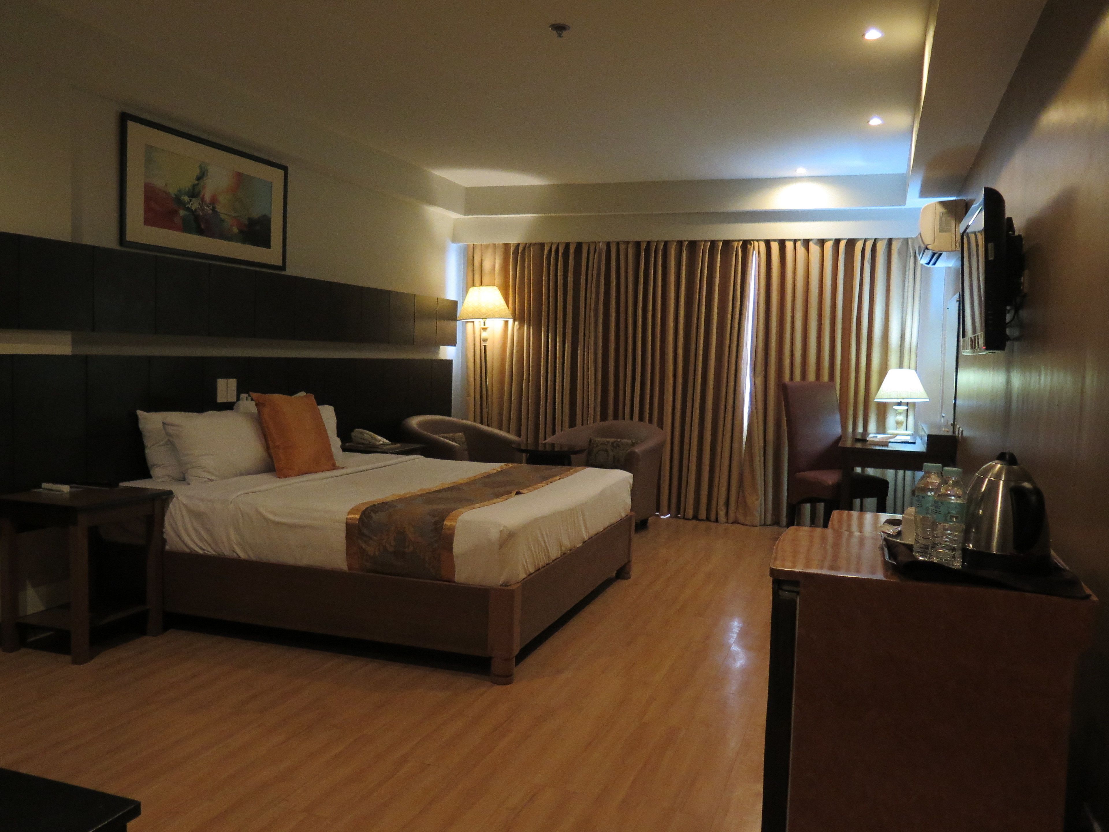 Une chambre d’hôtel comprenant un lit, des tables de chevet, un bureau avec une chaise, une lampe et un téléviseur fixé au mur.