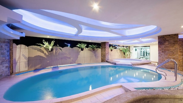 A modern indoor swimming pool with a curved design, surrounded by a stone wall and a wooden fence. - The Pinnacle Hotel and Suites (Davao)