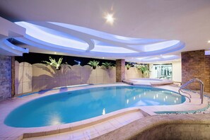 A modern indoor swimming pool with a curved design, surrounded by a stone wall and a wooden fence. - The Pinnacle Hotel and Suites (Davao)