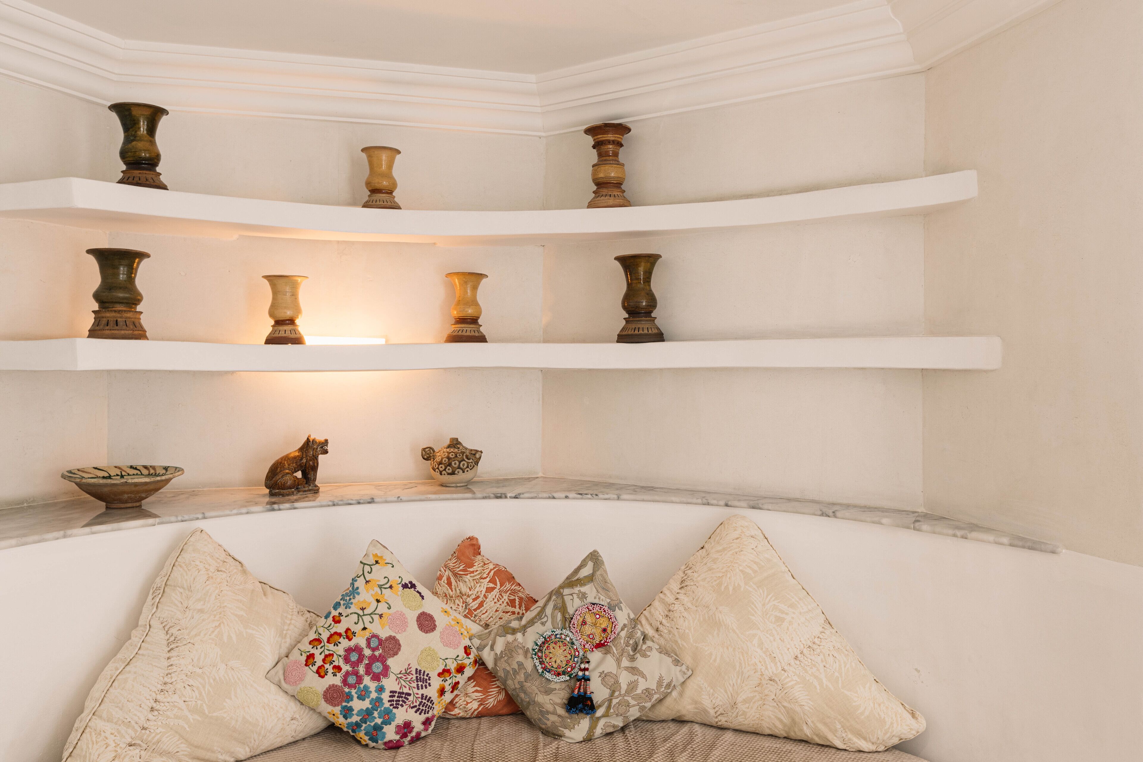 A corner with a white wall, a shelf with decorative vases, and a cushioned bench with patterned cushions.