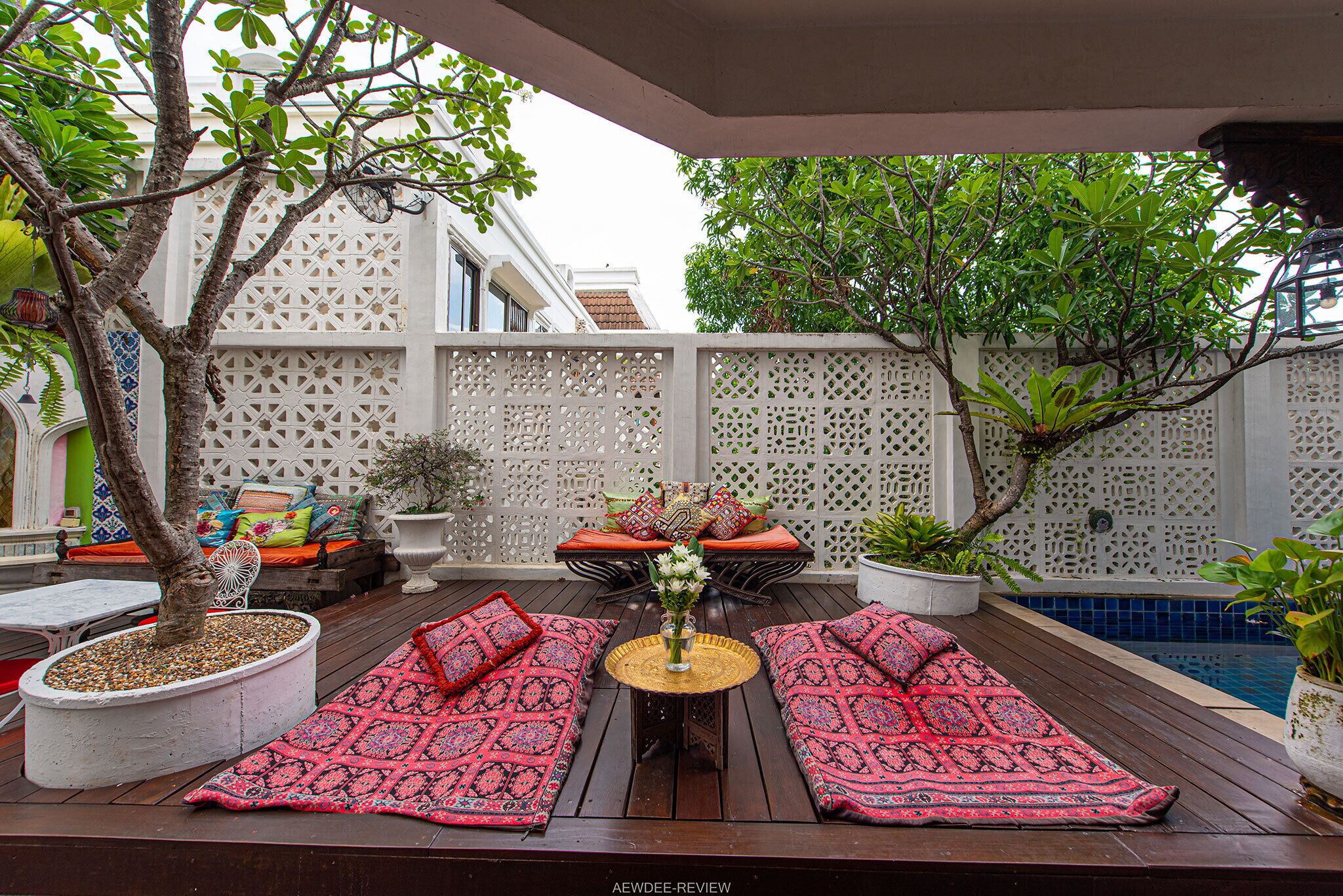 A wooden deck with two red patterned sofas, a small table with a vase of flowers, and a white lattice fence in the background.