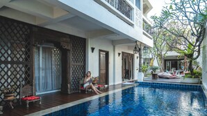 A poolside area with a person sitting by the pool, wooden deck, and a view of the pool. - At Niman Conceptual Home (Chiang Mai)