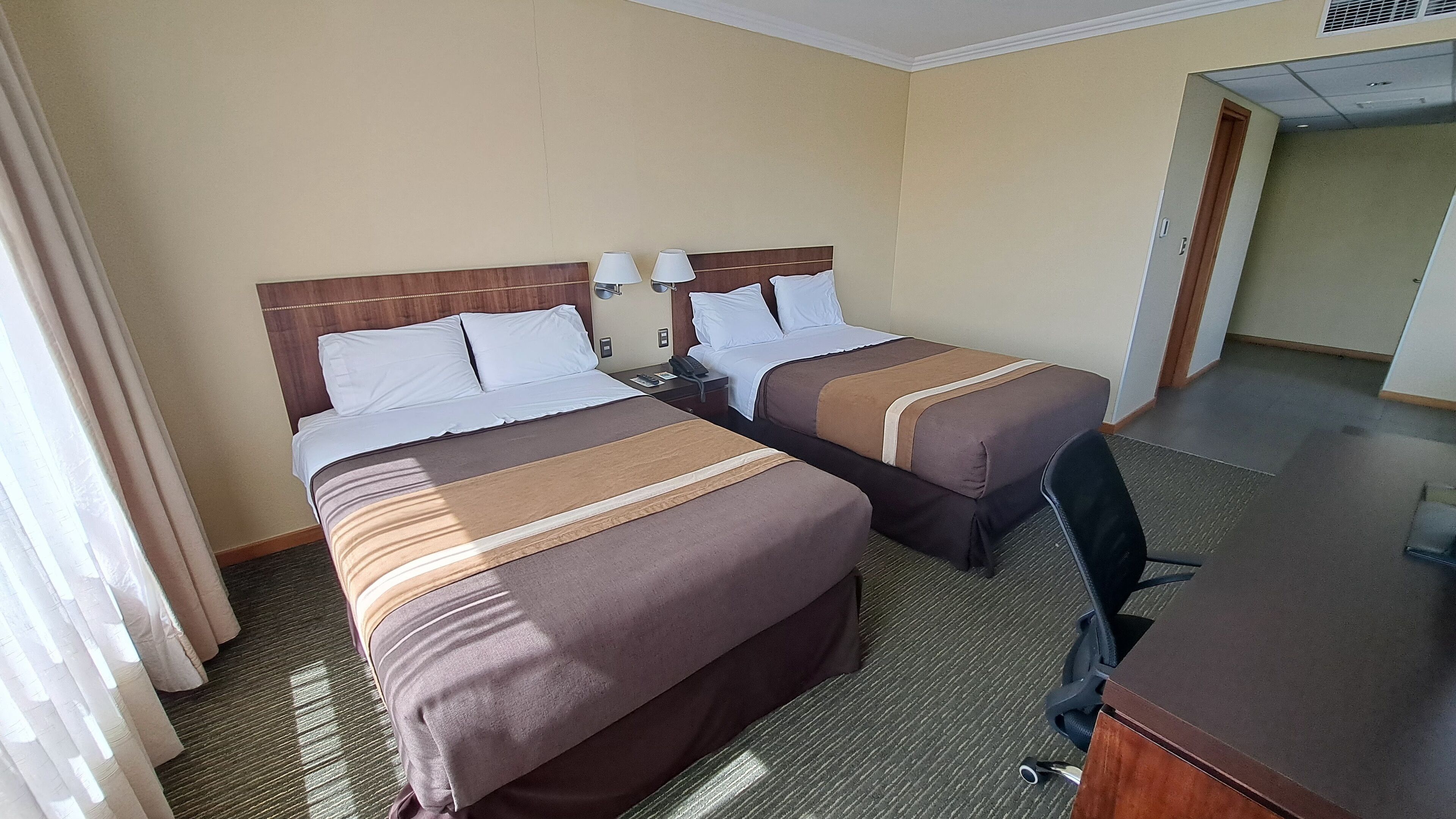 A hotel room with two beds, a desk, and a chair.