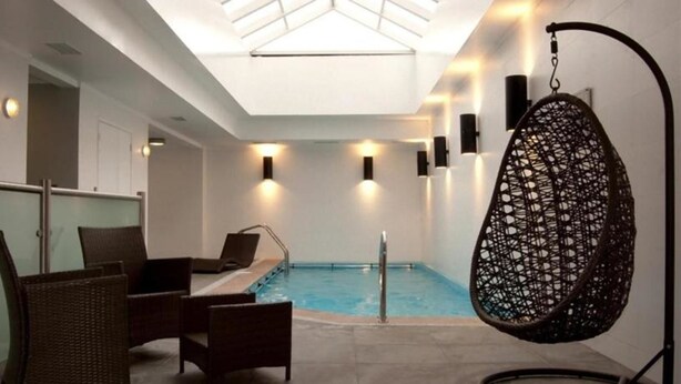 A modern indoor pool area with a glass ceiling, lounge chairs, and a hanging chair.