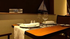 A dining table set with plates, cutlery, and wine glasses, with a sailboat model on the wall and a salt shaker on the table.