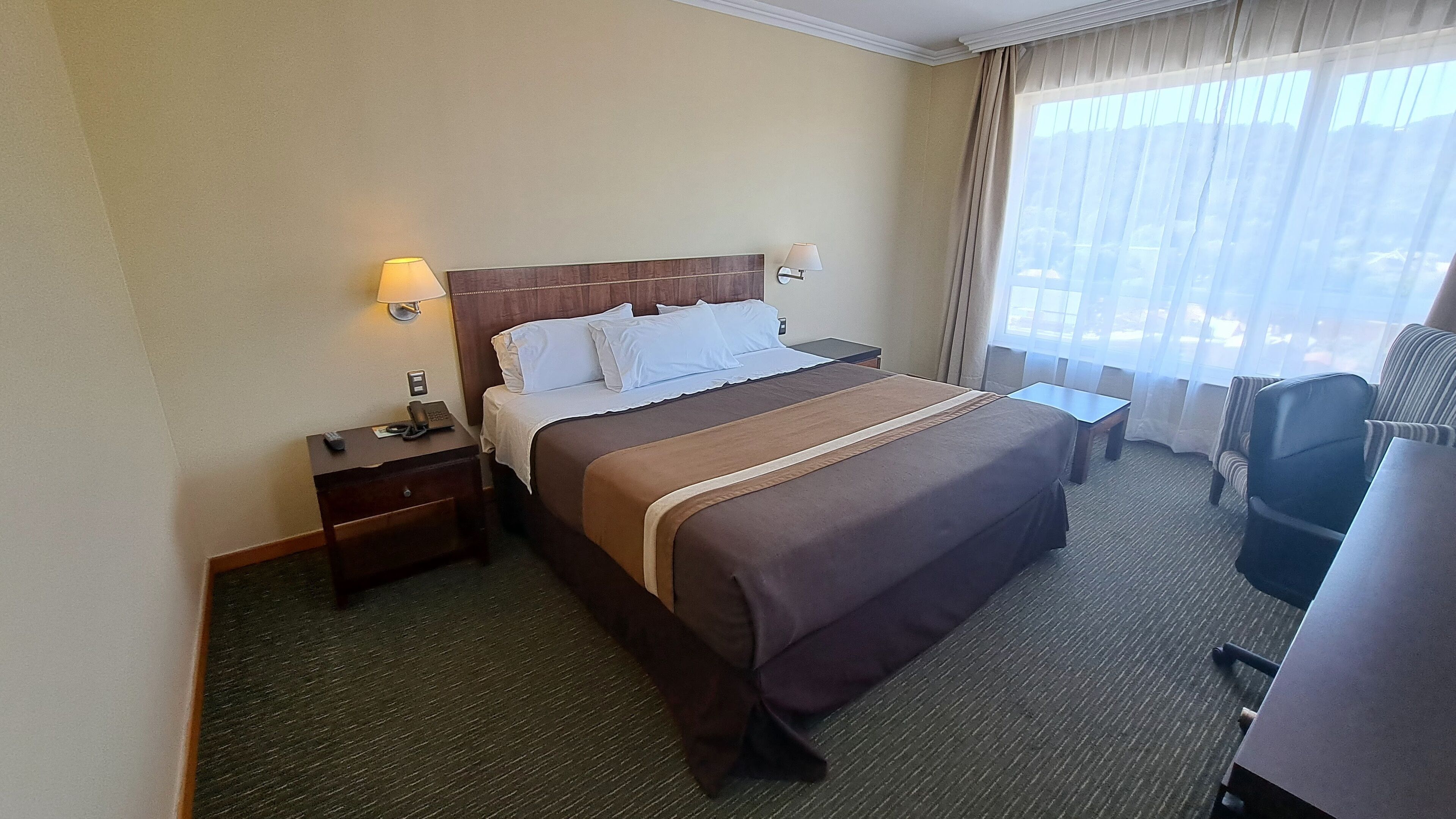 A hotel room with a large bed, a desk, a chair, and a window with curtains.