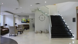 A modern lobby with a staircase, seating area, and a large wall clock.