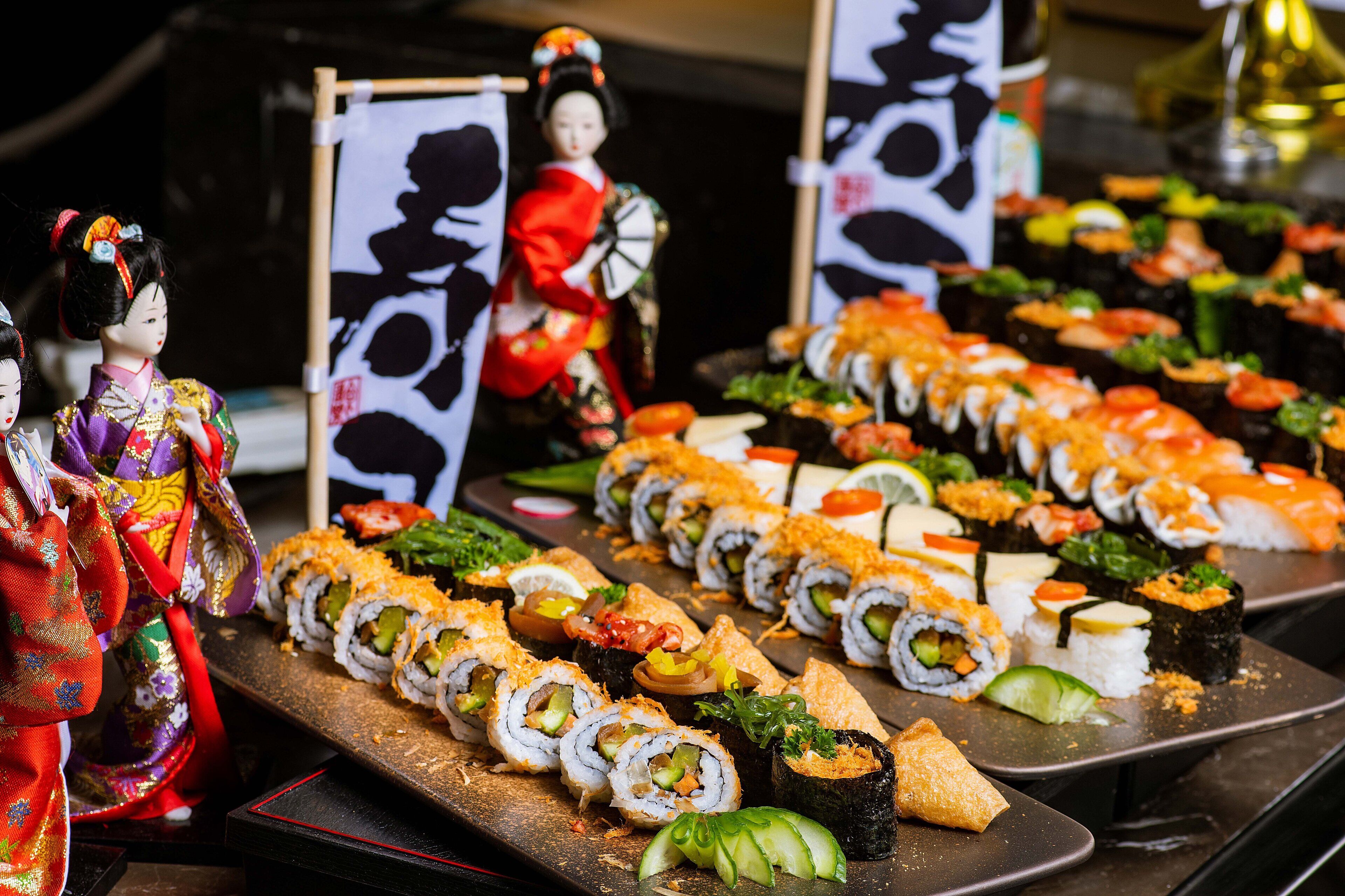 A sushi platter with various types of sushi and a traditional Japanese doll in the background.