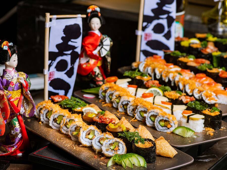 A sushi platter with various types of sushi and a traditional Japanese doll in the background.