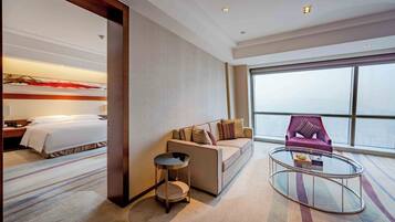 A hotel room with a bed, a sofa, a round coffee table, and a view of the city.