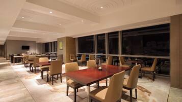 A spacious dining area with multiple tables and chairs, large windows, and a modern ceiling design.