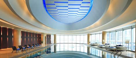 A modern indoor swimming pool with a curved ceiling and seating area.