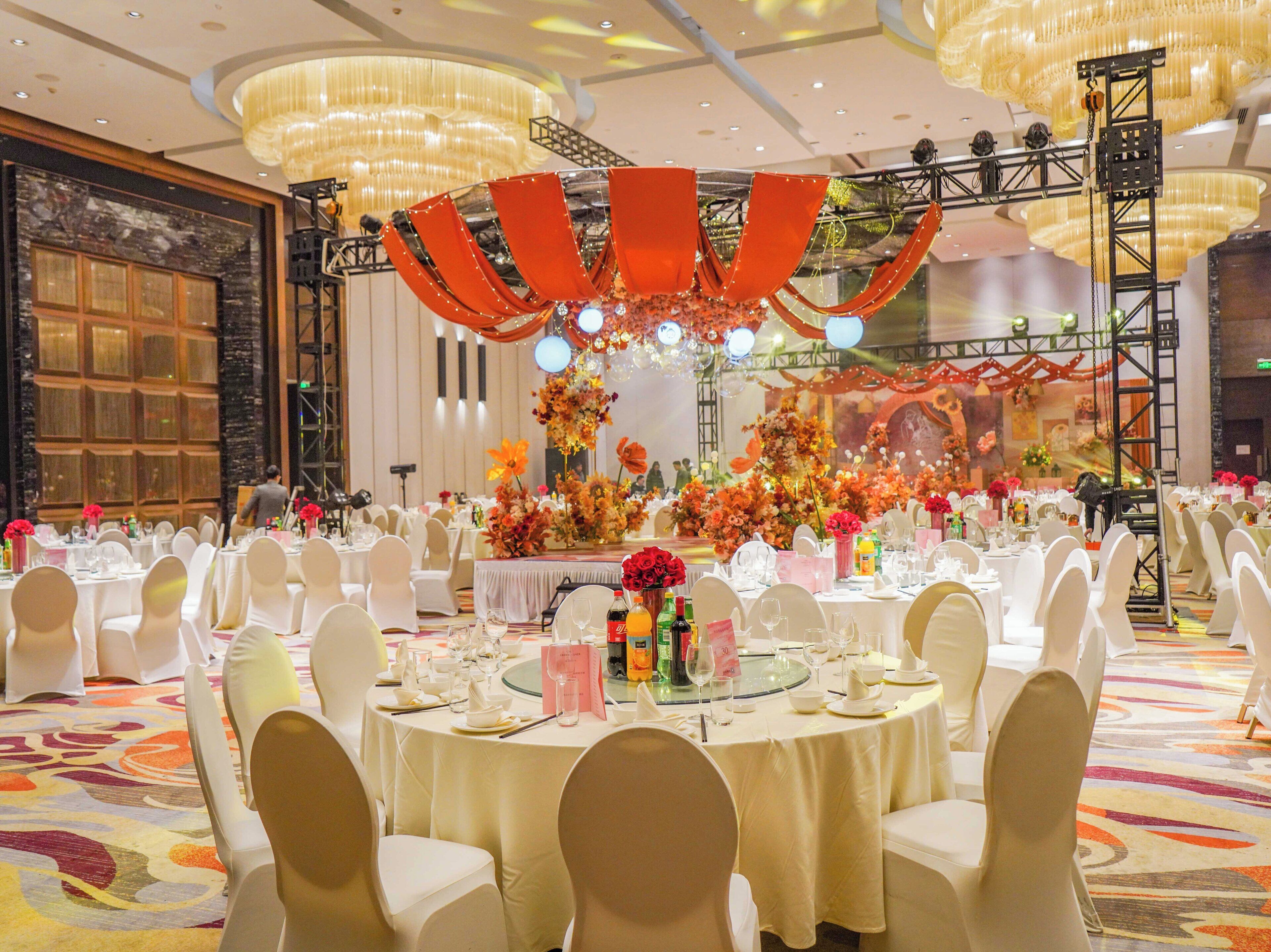 Une salle de banquet avec des tables rondes, des chaises blanches et une scène décorée de fleurs.