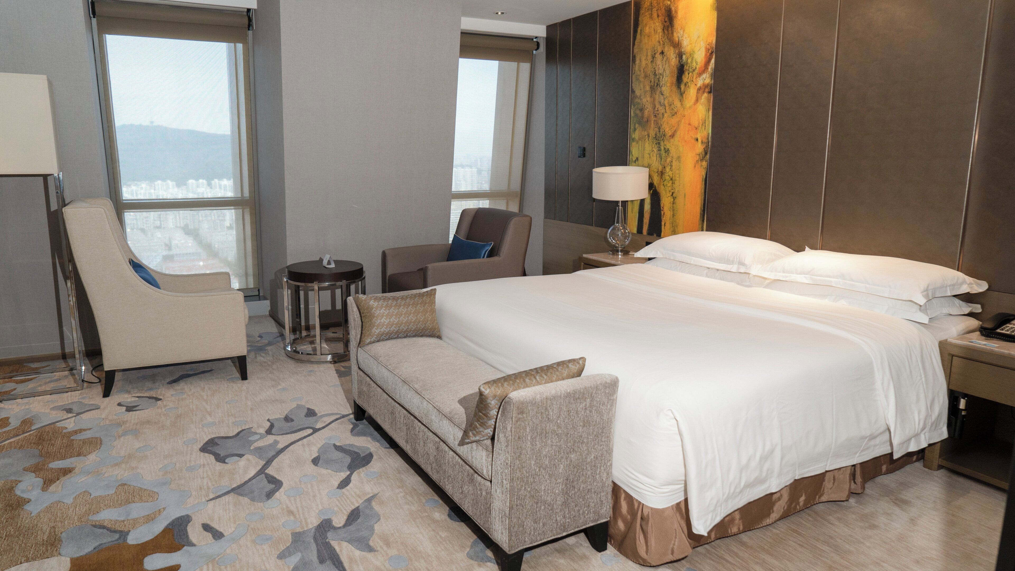 A hotel room with a large bed, a sofa, a chair, a small table, and a lamp.