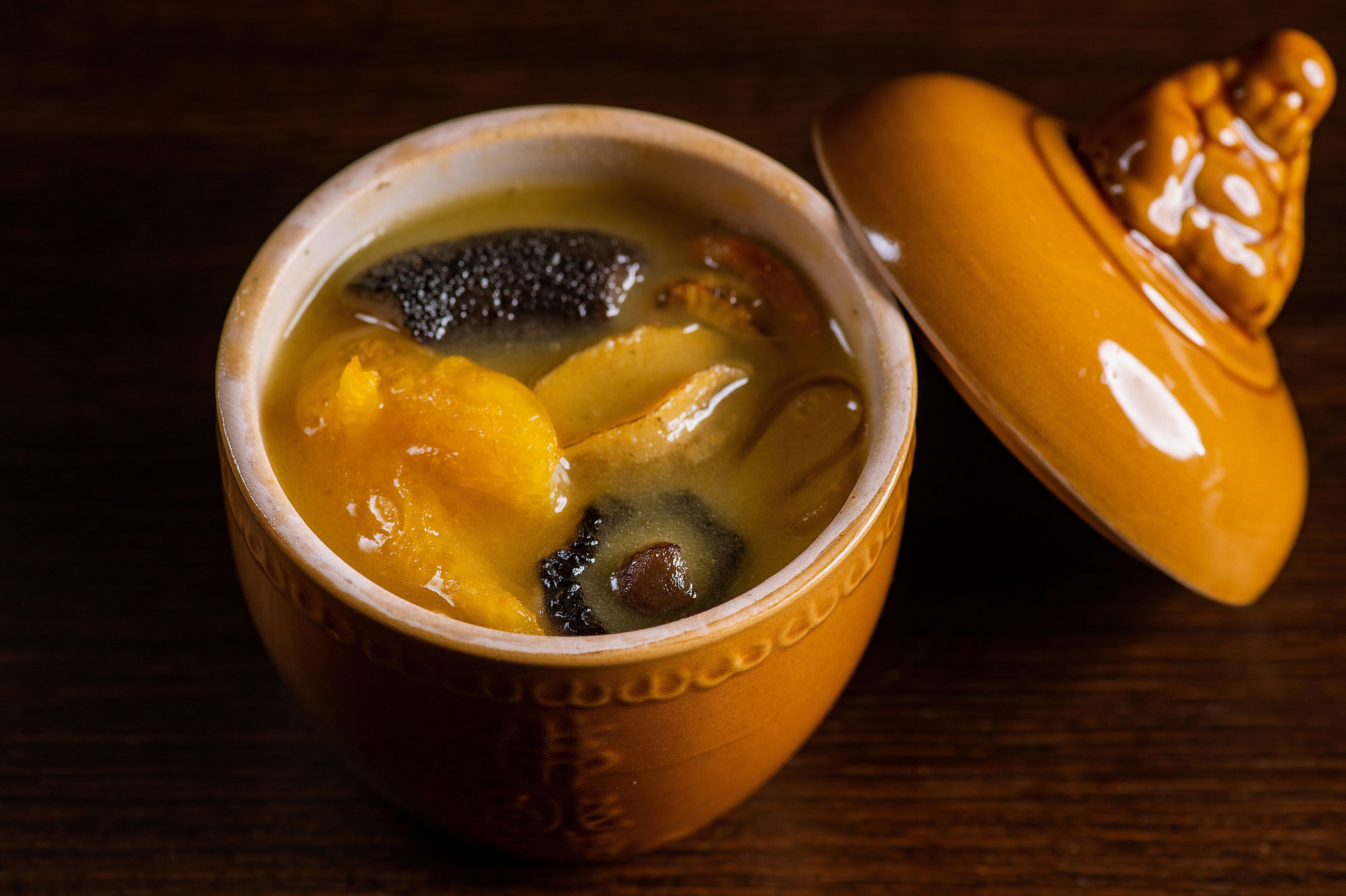 Un tazón de cerámica con tapa que contiene una sopa con ingredientes visibles como champiñones y patatas.