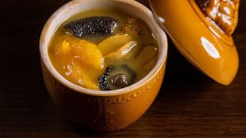 Un tazón de cerámica con tapa que contiene una sopa con ingredientes visibles como champiñones y patatas.
