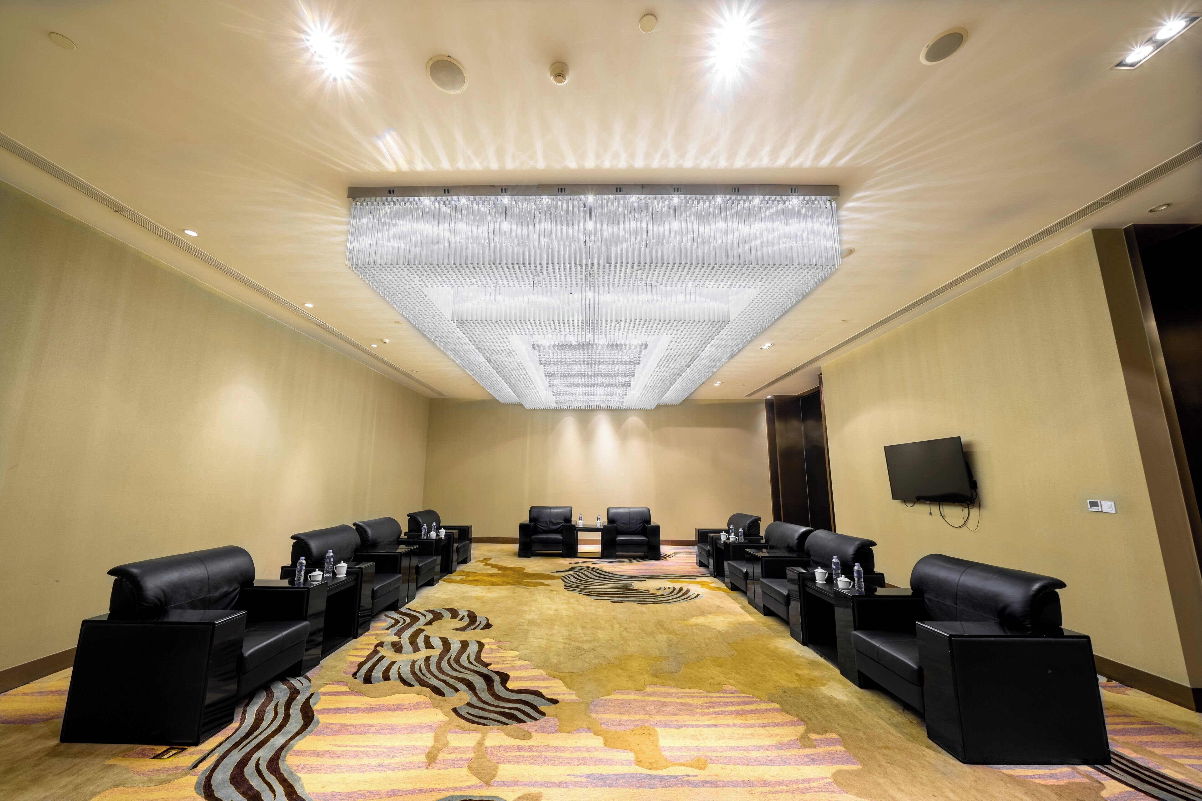 A conference room with a large, patterned carpet, black leather sofas, and a ceiling light fixture.