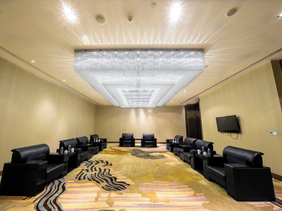 A conference room with a large, patterned carpet, black leather sofas, and a ceiling light fixture.